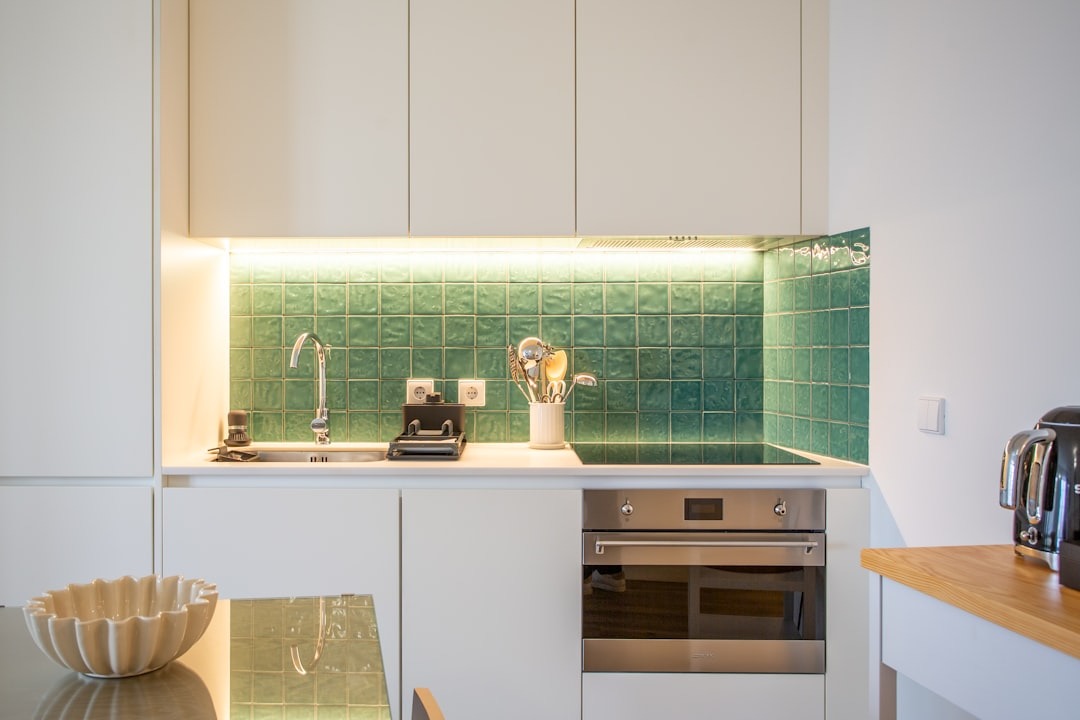 Modern kitchen with white cabinets and green tiled backsplash.